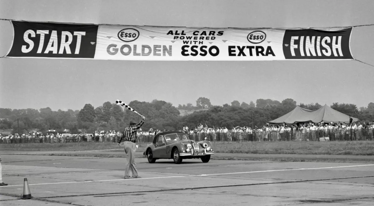 Denise McCluggage takes the checkered flag at Montgomery, New York, in August 1956—her competition debut and first race victory. Period photograph by Ozzie Lyons, courtesy Pete Lyons.
